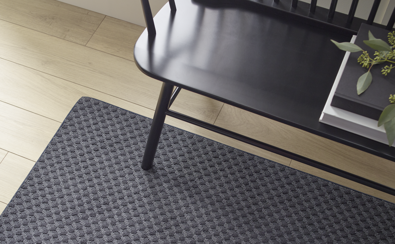 dark grey area rug runner under black bench in hallway with light wood floors